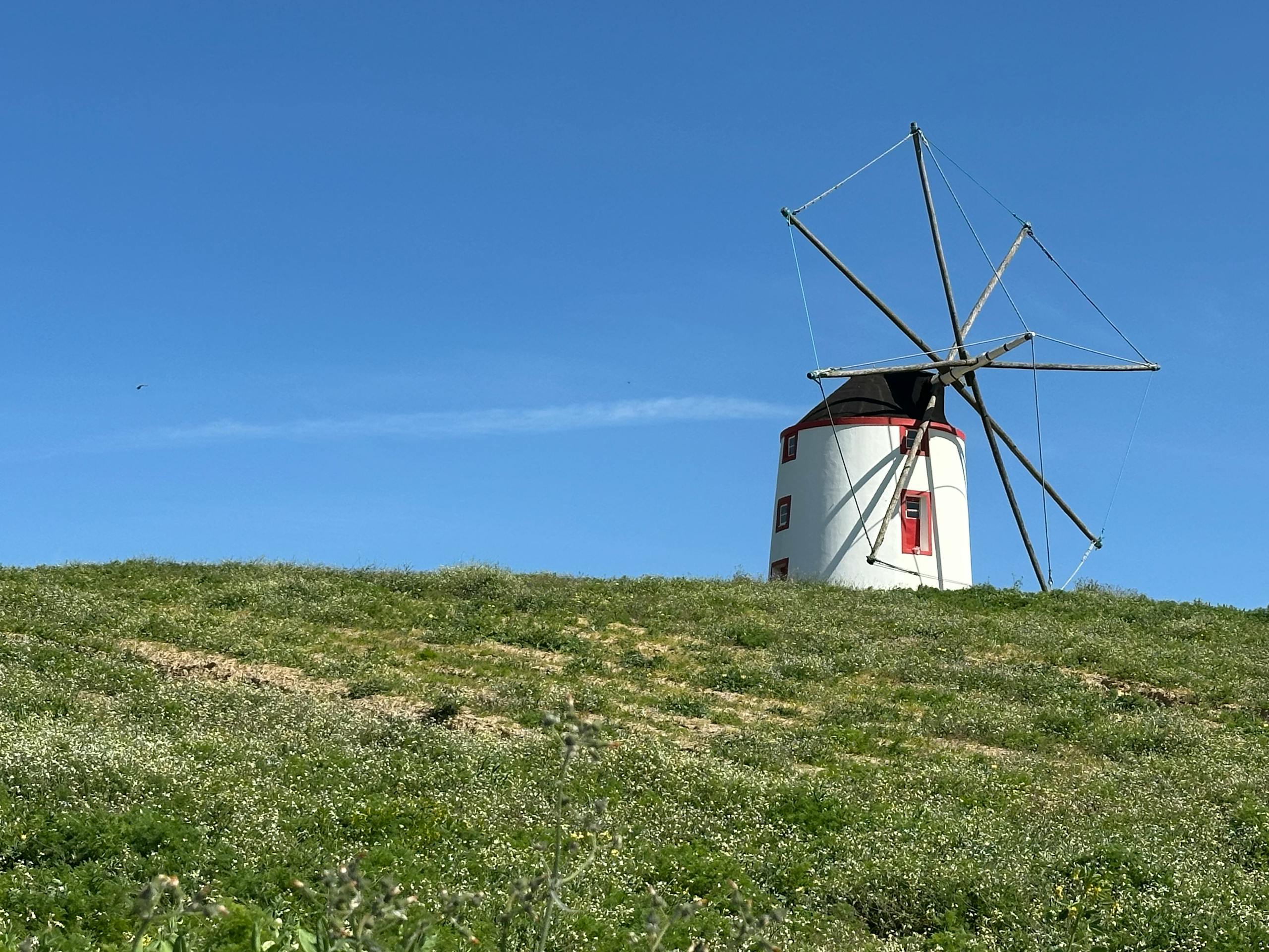A traditional windmill stands majestically on a grassy hill under a clear blue sky in Portugal.